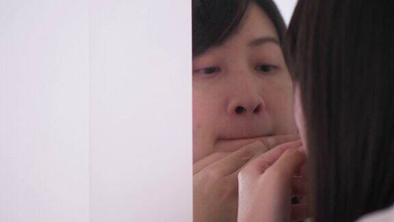 一名泰国妇女正在镜子旁挤她脸上和嘴上的痘痘