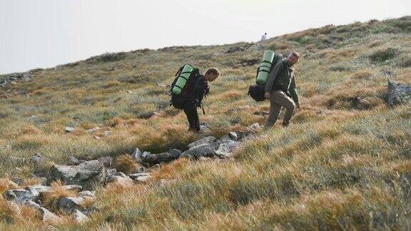 两名游客一男一女正背着巨大的旅游背包沿着山坡行走