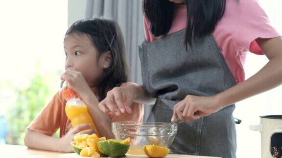 亚洲女孩教她的妹妹如何挤橙汁在家里处理甜果冻