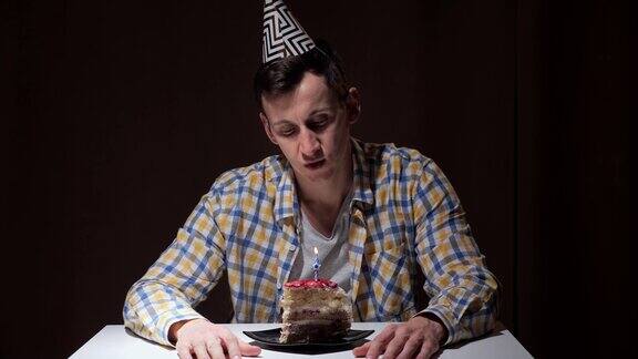 戴着生日帽的心烦意乱的人看着蛋糕吹灭了蜡烛