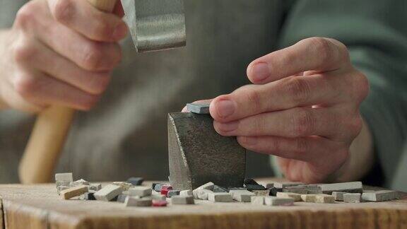 男性用一把特制的锤子把马赛克砖敲成两半为铺设马赛克图案而准备的石材在创意工作室手工制作关闭了慢动作