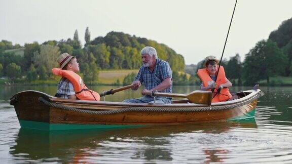 爷爷和孙子们坐在公园里的湖上划船钓鱼