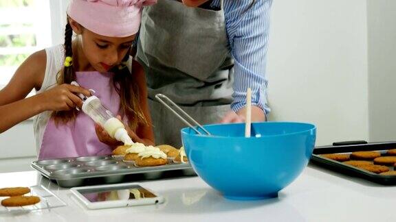 妈妈帮小女孩用奶油装饰纸杯蛋糕