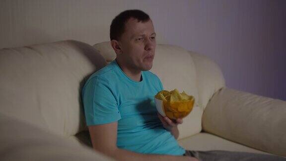 有魅力的男人坐在沙发上看电视吃着薯片