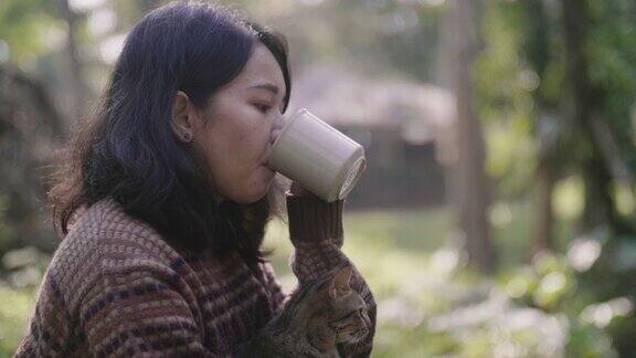亚洲女孩坐在瀑布附近喝一些热咖啡在美好的日子