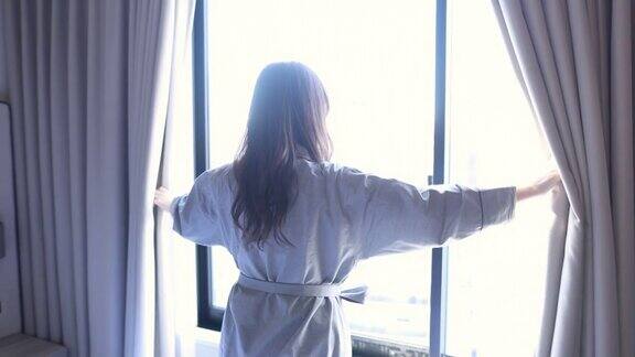 清晨一位年轻女子在酒店房间里拉开窗帘