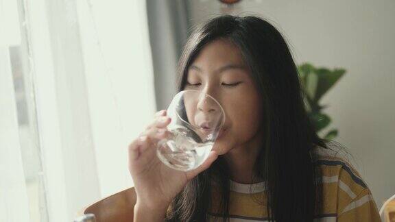 亚洲女孩喝一杯水坐在家里靠窗的地方生活理念