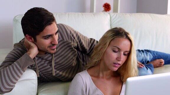 一对快乐的年轻夫妇坐在沙发上用笔记本电脑