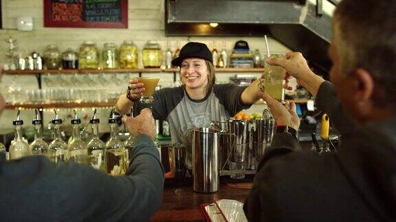 一个白种女调酒师在她三十多岁的双手微笑两个白种男人在酒吧工作时他们的鸡尾酒