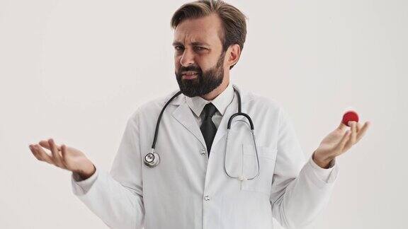 困惑的男医生用听诊器看着瓶子里的药丸一边用手打手势