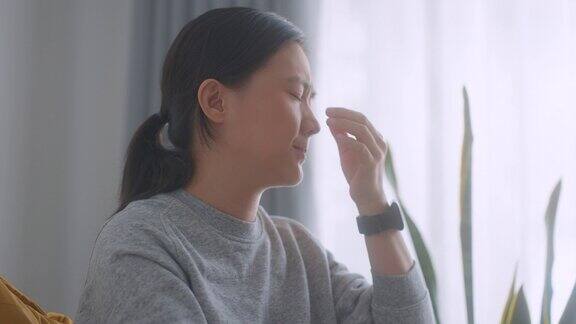 一位亚洲妇女坐在家里客厅的扶手椅上眼睛痛得难受