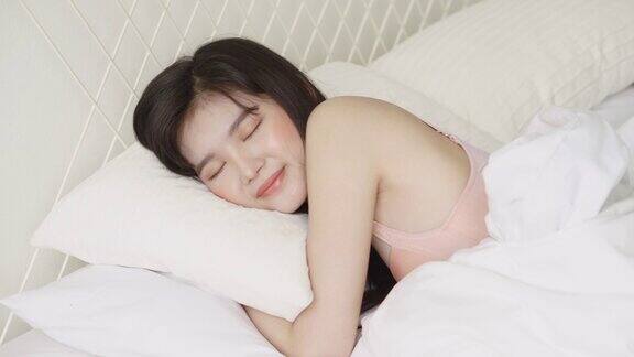 年轻的亚洲女子躺在床上头枕在枕头上在卧室移动平移相机舒适和快乐女孩以放松和休闲为健康生活方式