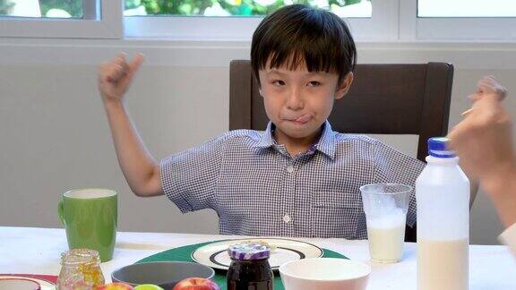 可爱快乐的年轻亚洲男孩早上在家吃早餐和喝牛奶;看相机