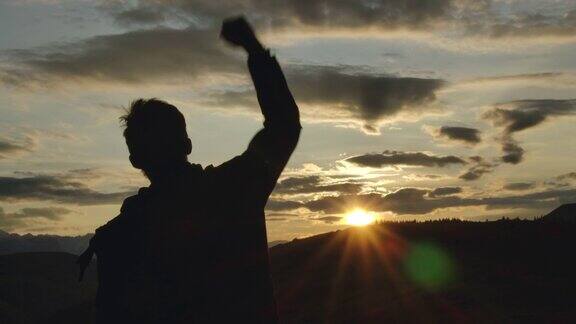 一个成功的快乐旅行人站在快乐和举起手快乐的剪影30岁的男人看风景日落天空背后的山冒险旅行徒步男人的手在山上举起特写