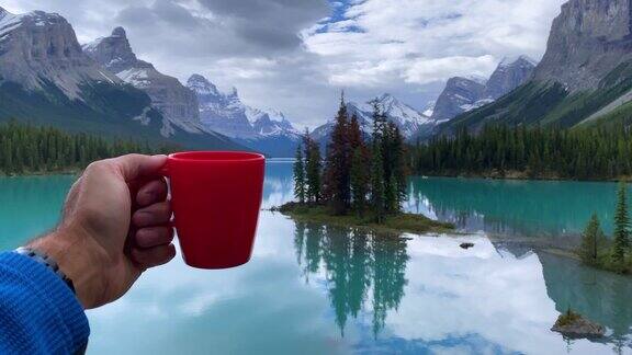 加拿大阿尔伯塔省贾斯帕国家公园玛琳湖的精灵岛一只展示咖啡杯的人手
