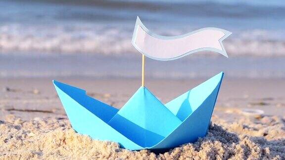 蓝色的纸船在海边的沙滩上在一个阳光明媚的夏天在小船上文字要有空格小船从纸上在沙滩上靠近海浪概念旅游旅游度假休息度假