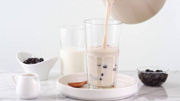 将奶茶倒入玻璃杯中配以台湾流行的木薯珍珠泡放在明亮的大理石桌上和白色托盘上这是自制4k视频拍摄