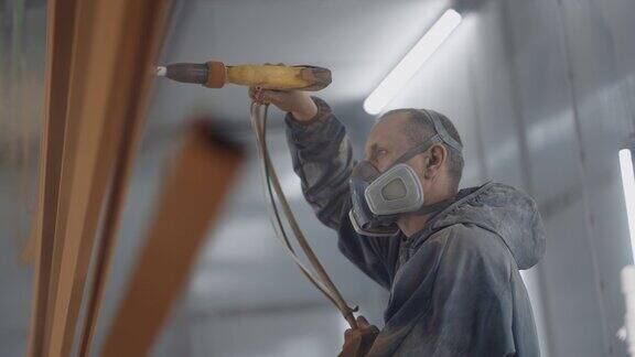 一个戴着呼吸器的人正在用粉末喷涂法喷涂金属绘画店油漆工用喷枪喷涂油漆