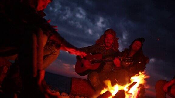 在冬季沙滩派对上为朋友们弹吉他的男人