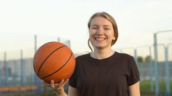 年轻的金发女孩拿着篮球看起来积极和快乐的站着微笑着自信的微笑露出牙齿