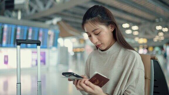 年轻的亚洲游客坐在空空如也的候机大厅里浏览智能手机