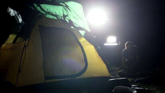 两名男子在探险越野车的灯光下搭建帐篷的夜景