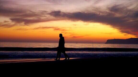 慢镜头里一对情侣在日落时分的海滩上散步