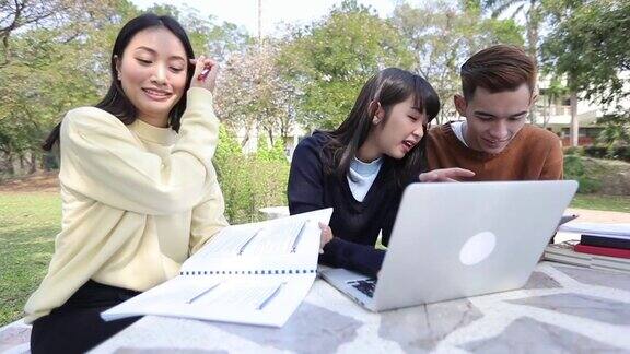 一群亚洲大学生坐在草地上微笑一起在公园里工作和阅读(慢镜头)