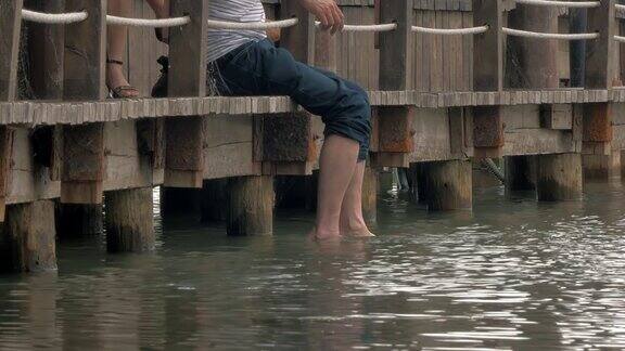 一个人坐在木码头上把脚挂在湖里