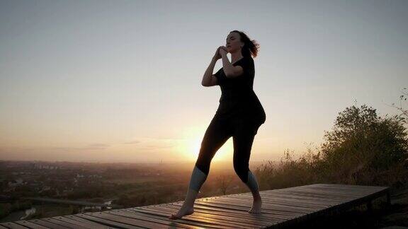 日落时分女子站在瑜伽垫上做瑜伽伸展运动广角镜头画面