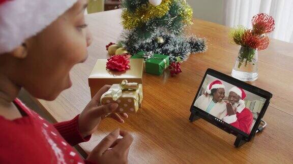 非裔美国妇女戴着圣诞帽用平板电脑进行圣诞视频通话屏幕上有一对夫妇