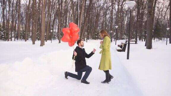 在一个冬日的公园里一名年轻男子单膝跪地向他的漂亮女子求婚