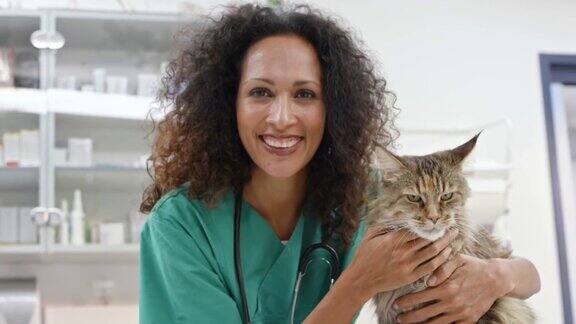一位女兽医对着镜头微笑抚摸着办公室检查台上的一只缅因猫