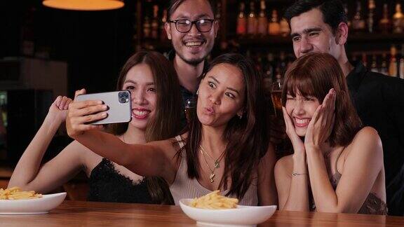 年轻的亚洲朋友在酒吧喝酒看着相机自拍微笑