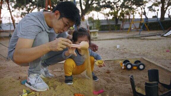 亚裔父亲和女儿在公园里玩可爱的幼童喜欢在周末和父母一起玩沙箱家庭在公园