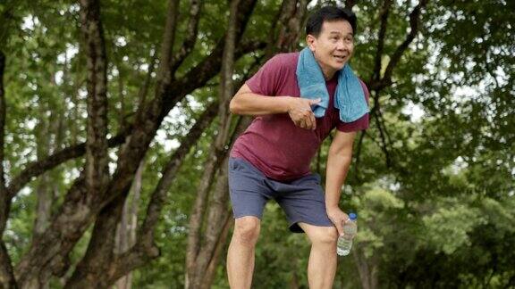 亚洲中年男子在公园跑步和休息站在树下和休息后锻炼身体健康疲惫疲惫男子医疗保健人寿保险计划锻炼日常
