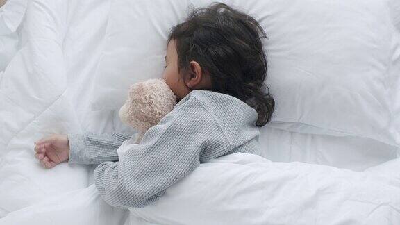 一个亚洲小女孩在卧室里睡觉抱着泰迪熊