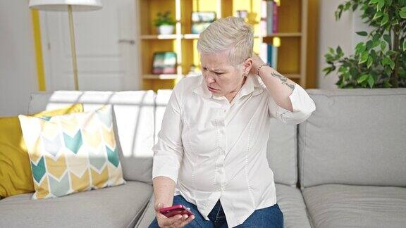 白发苍苍的中年妇女在家用智能手机治疗颈椎疼痛