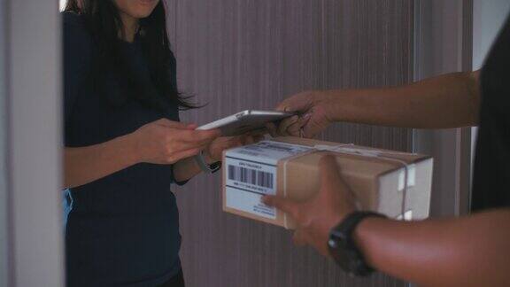 一名年轻女子收到邮递员寄来的包裹并签上名