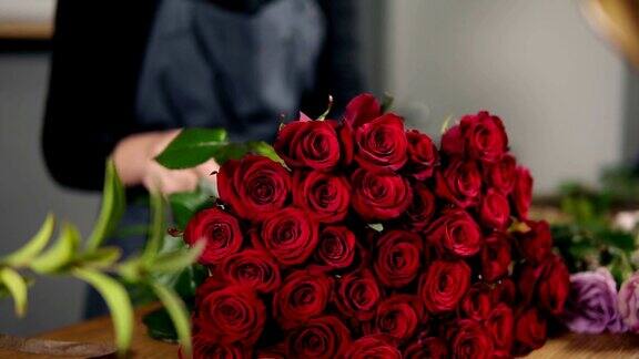 桌上摆着一束完美的红玫瑰近距离观看的手的女性花商安排现代花束使用美丽的红玫瑰在花店Slowmotion拍摄