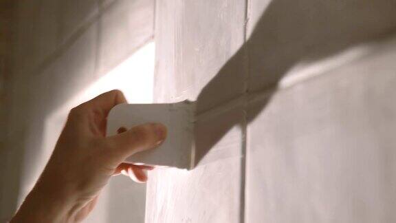 在浴室墙上贴瓷砖的工人他的手把瓷砖放在粘合剂上