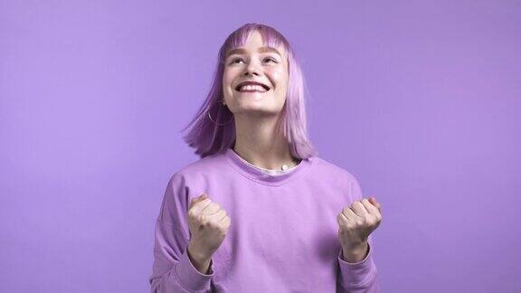 染了紫色头发的女人非常高兴和快乐她表现出胜利的姿态她达到了结果目标惊喜兴奋快乐的女士在紫罗兰工作室背景大奖