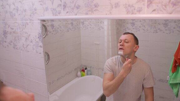 小伙子早上站在浴室附近的镜子前刮胡子镜头移动