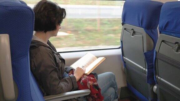 白人妇女坐在火车靠窗的位置看书火车在站台停