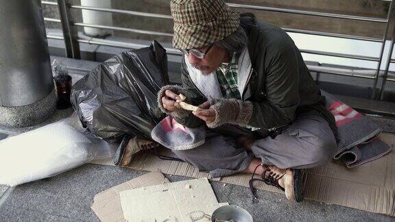 倾斜:无家可归的人吃着食物坐在人行道上