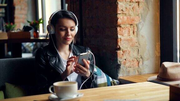 快乐的女学生在咖啡厅用手机听耳机听音乐