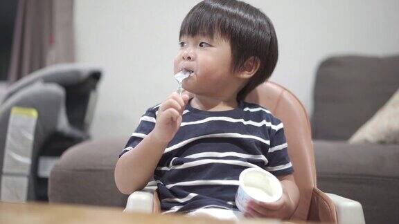 亚洲小男孩在家里的客厅里独自吃酸奶