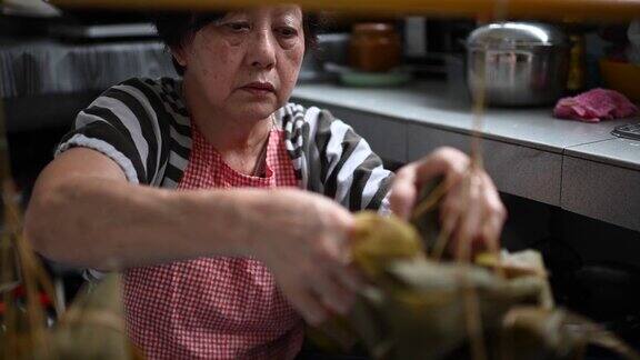 一位年长的亚洲华人妇女在她的厨房里准备粽子把配料包好为端午节做准备