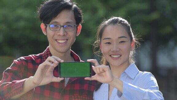 年轻的亚洲夫妇在户外展示手机