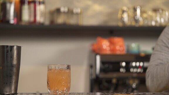 柜台上放着一个空白的杯子调酒师从柜台上拿起摇酒器将葡萄柚汁倒进去并在杯口放上一片葡萄柚片